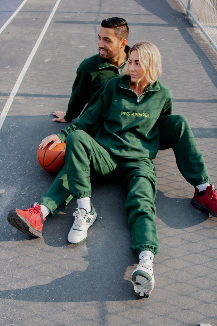 Fashionable couple lounging on an outdoor basketball court in green tracksuits, enjoying a sunny day.