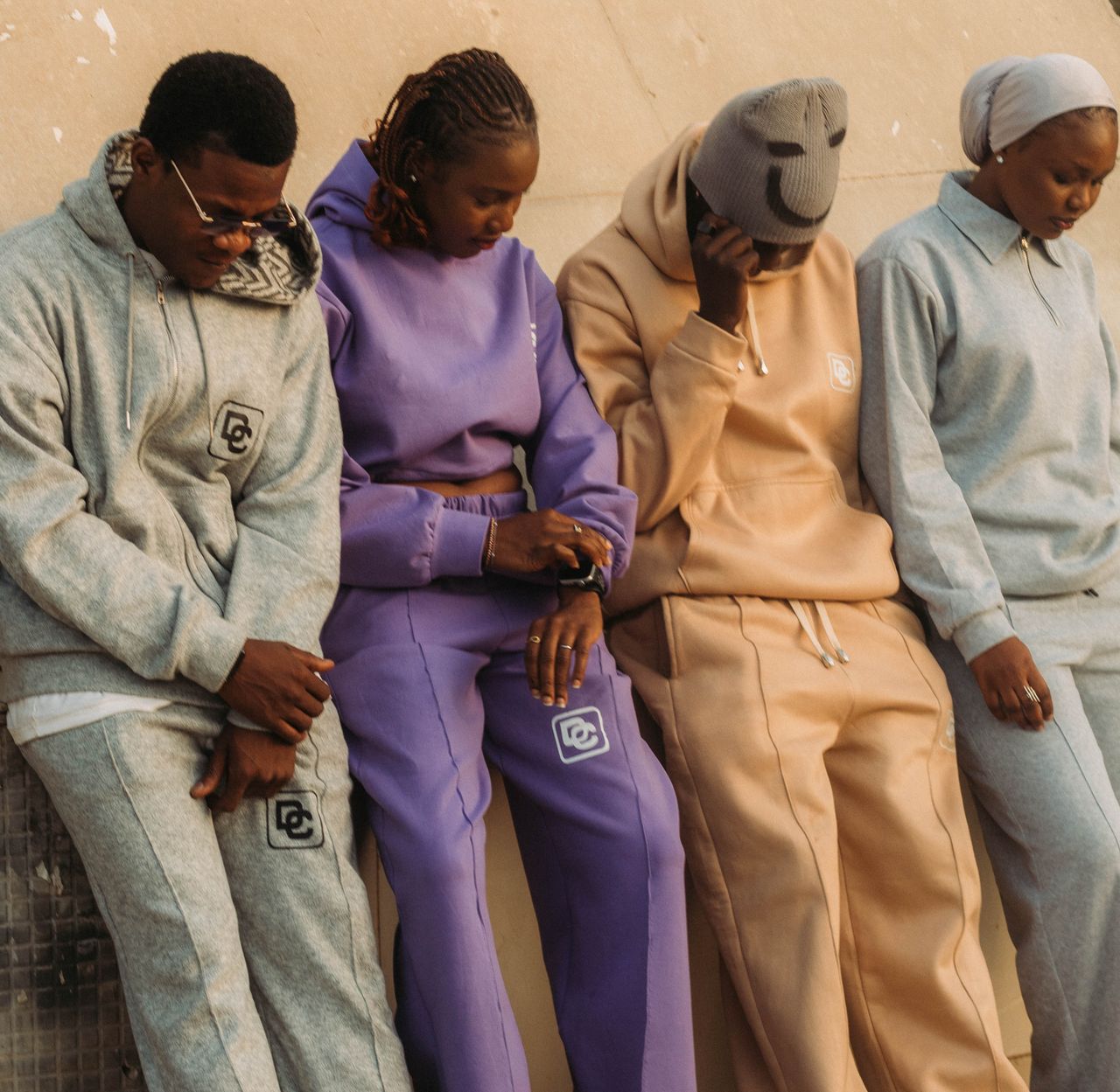 A group of adults in trendy, colorful tracksuits leaning against a wall outdoors.